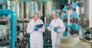 Female worker inspecting water bottle on production line in spring water factory
