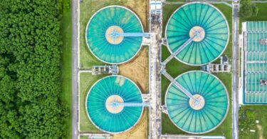 Aerial view of large circular wastewater treatment tanks surrounded by greenery