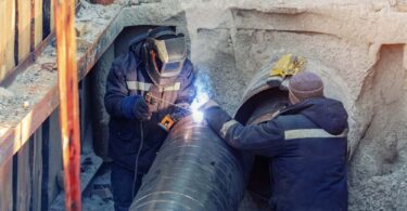 Engineers welding a large underground water pipe during replacement works to improve water safety.