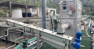 Mechanical screening equipment installed at an outdoor wastewater treatment plant, showing stainless steel screening unit, conveyor and associated pipework.