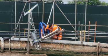 Technicians installing a Landia JetMix aeration system on the edge of a live effluent tank.