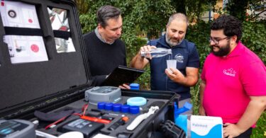 Richard King, Willie Plowman, and Adam Ali testing water samples with Palintest’s Wagtech Potalab+ water testing system beside the River Dart.