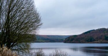 Scammonden Reservoir in winter, with still water, bare trees and rolling hills beneath an overcast sky.