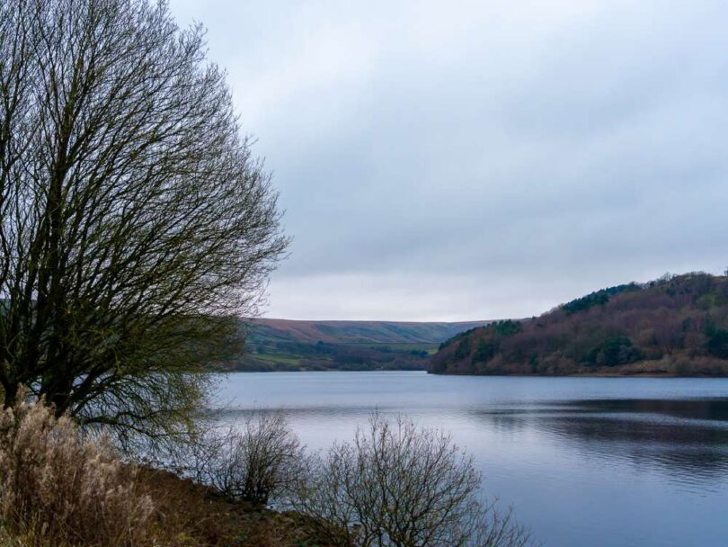 Scammonden Reservoir in winter, with still water, bare trees and rolling hills beneath an overcast sky.