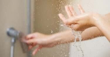 Hands under a running shower demonstrating household water use and water efficiency.