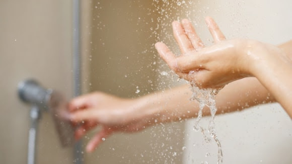 Hands under a running shower demonstrating household water use and water efficiency.