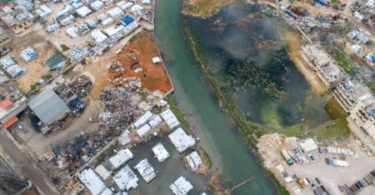 Water infrastructure damage in conflict zone showing polluted river and destroyed urban water systems
