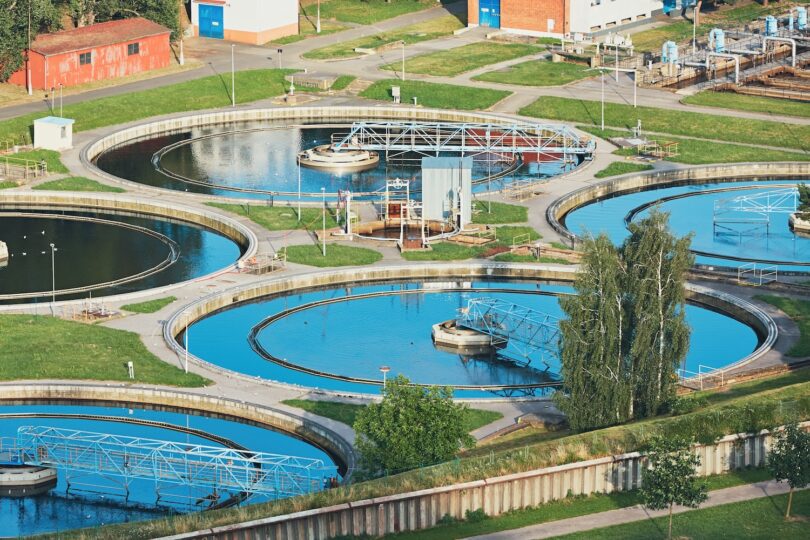 Aerial view of a wastewater treatment plant with circular clarifiers and interconnected systems, representing infrastructure where digital monitoring and optimisation technologies are applied.