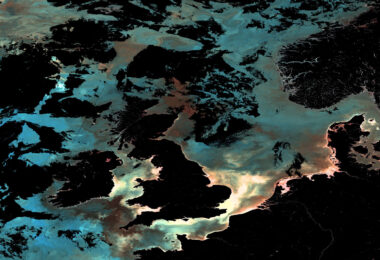 Ocean-colour satellite image of the UK and surrounding north-east Atlantic waters, showing phytoplankton, sediment and dissolved organic matter patterns captured by Copernicus Sentinel-3.