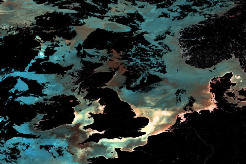 Ocean-colour satellite image of the UK and surrounding north-east Atlantic waters, showing phytoplankton, sediment and dissolved organic matter patterns captured by Copernicus Sentinel-3.