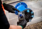 Worker using a smartphone to photograph a blue pipe flange during pipeline quality assurance