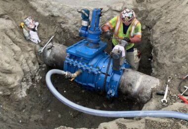 Worker installing a blue insertion valve on a large-diameter fire suppression pipeline in an excavated trench