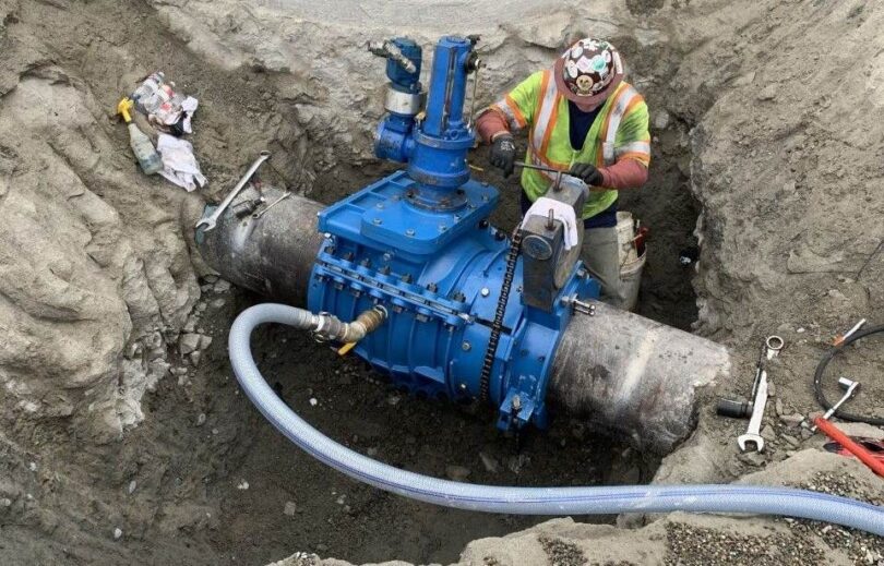 Worker installing a blue insertion valve on a large-diameter fire suppression pipeline in an excavated trench