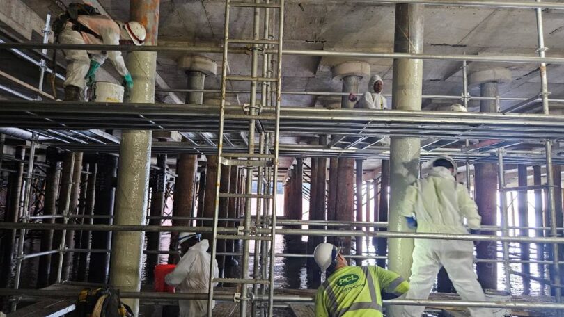 Workers applying protective coating to wharf piles during the Nashville Wharf rehabilitation project