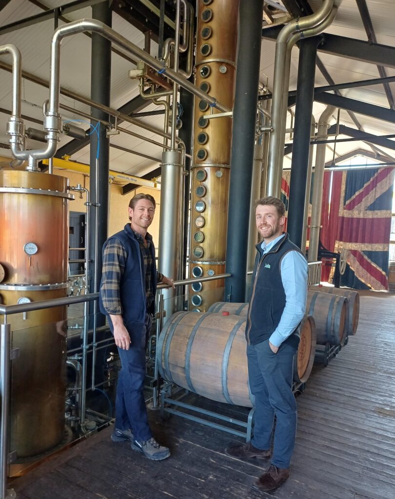 Josh Edge and Will Skinner inside Rosemaund Farm Distillery beside production equipment and whisky casks
