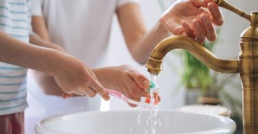 Child brushing teeth while tap water runs into a sink