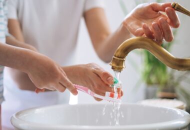 Child brushing teeth while tap water runs into a sink