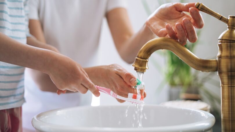Child brushing teeth while tap water runs into a sink