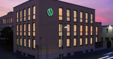 De Nora office building with the company’s illuminated green logo at dusk