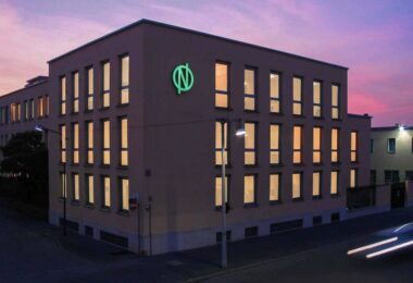 De Nora office building with the company’s illuminated green logo at dusk