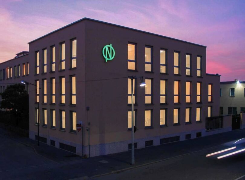 De Nora office building with the company’s illuminated green logo at dusk