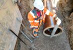 Construction worker positioning a vitrified clay sewer pipe in an excavated trench