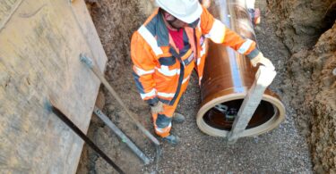 Construction worker positioning a vitrified clay sewer pipe in an excavated trench