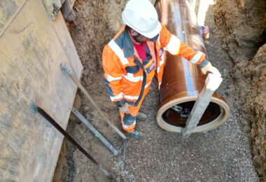 Construction worker positioning a vitrified clay sewer pipe in an excavated trench