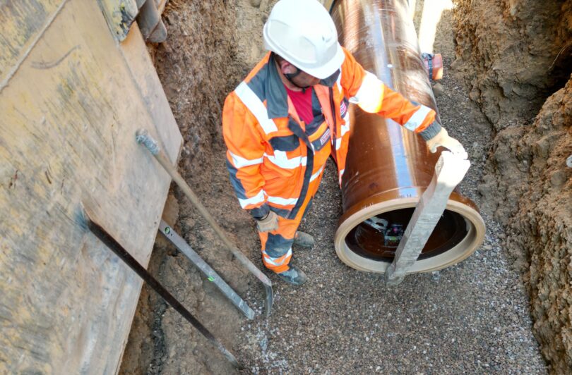 Construction worker positioning a vitrified clay sewer pipe in an excavated trench