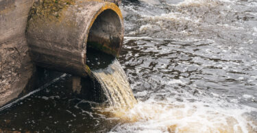 Dirty water flowing from a pipe into a river, illustrating environmental pollution.