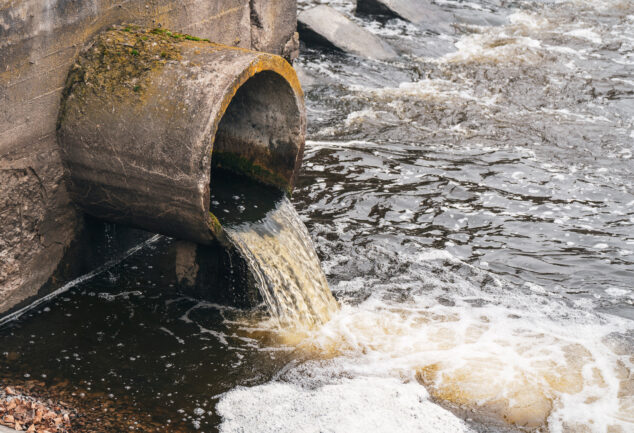 Dirty water flowing from a pipe into a river, illustrating environmental pollution.