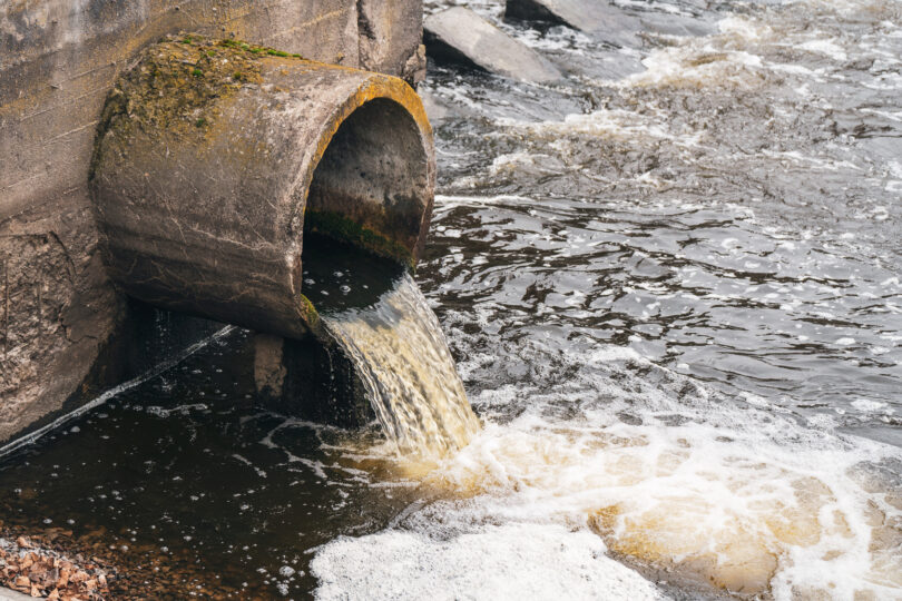 Dirty water flowing from a pipe into a river, illustrating environmental pollution.