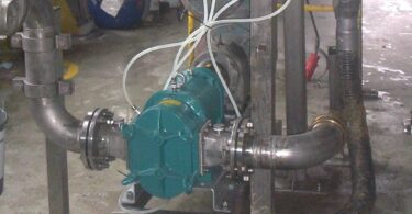 Teal rotary lobe pump on a steel frame, connected to stainless pipes, with a motor behind and a corrugated hose at right