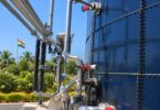 Stainless steel pipes, pump and red-handled valves along a large blue glass-fused steel tank, with an Indian flag in the back