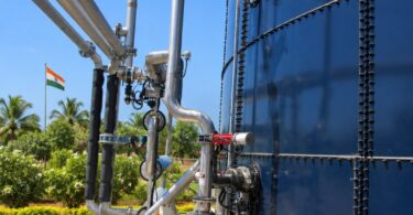 Stainless steel pipes, pump and red-handled valves along a large blue glass-fused steel tank, with an Indian flag in the back