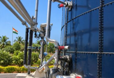 Stainless steel pipes, pump and red-handled valves along a large blue glass-fused steel tank, with an Indian flag in the back