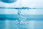 Water being poured into a glass of water, with soap bubbles forming.