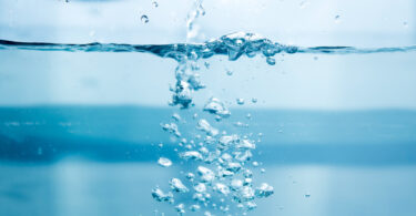 Water being poured into a glass of water, with soap bubbles forming.
