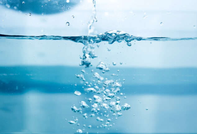 Water being poured into a glass of water, with soap bubbles forming.