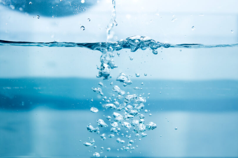Water being poured into a glass of water, with soap bubbles forming.