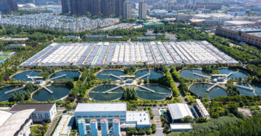 Sewage treatment plant with a solar power station, showing water treatment tanks and rows of solar panels.