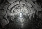 Curved underground tunnel draining water from soil, with light visible at the far end.