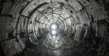 Curved underground tunnel draining water from soil, with light visible at the far end.