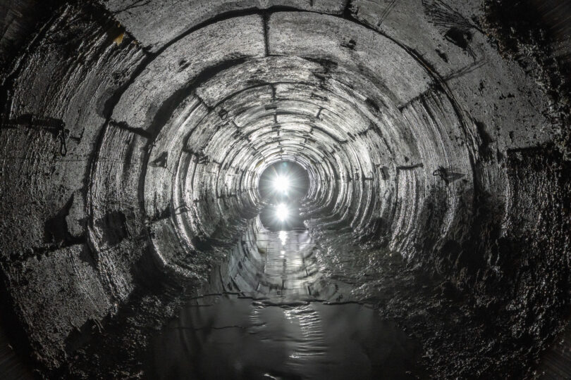 Curved underground tunnel draining water from soil, with light visible at the far end.
