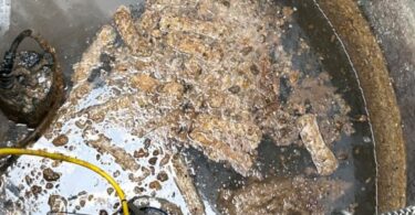 Looking down into a wet well where a mass of fatty, debris-laden clumps floats around a submersible pump and yellow hose
