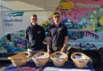 Two South West Water representatives standing behind a table with wicker baskets of information packs beside a branded van