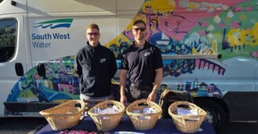 Two South West Water representatives standing behind a table with wicker baskets of information packs beside a branded van