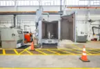Industrial equipment inside a manufacturing facility, including an open grey testing chamber containing a submersible pump, with yellow floor markings and orange safety cones.