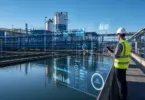 Worker in hard hat and safety vest holds a tablet beside a water treatment basin, with digital data panels overlaid